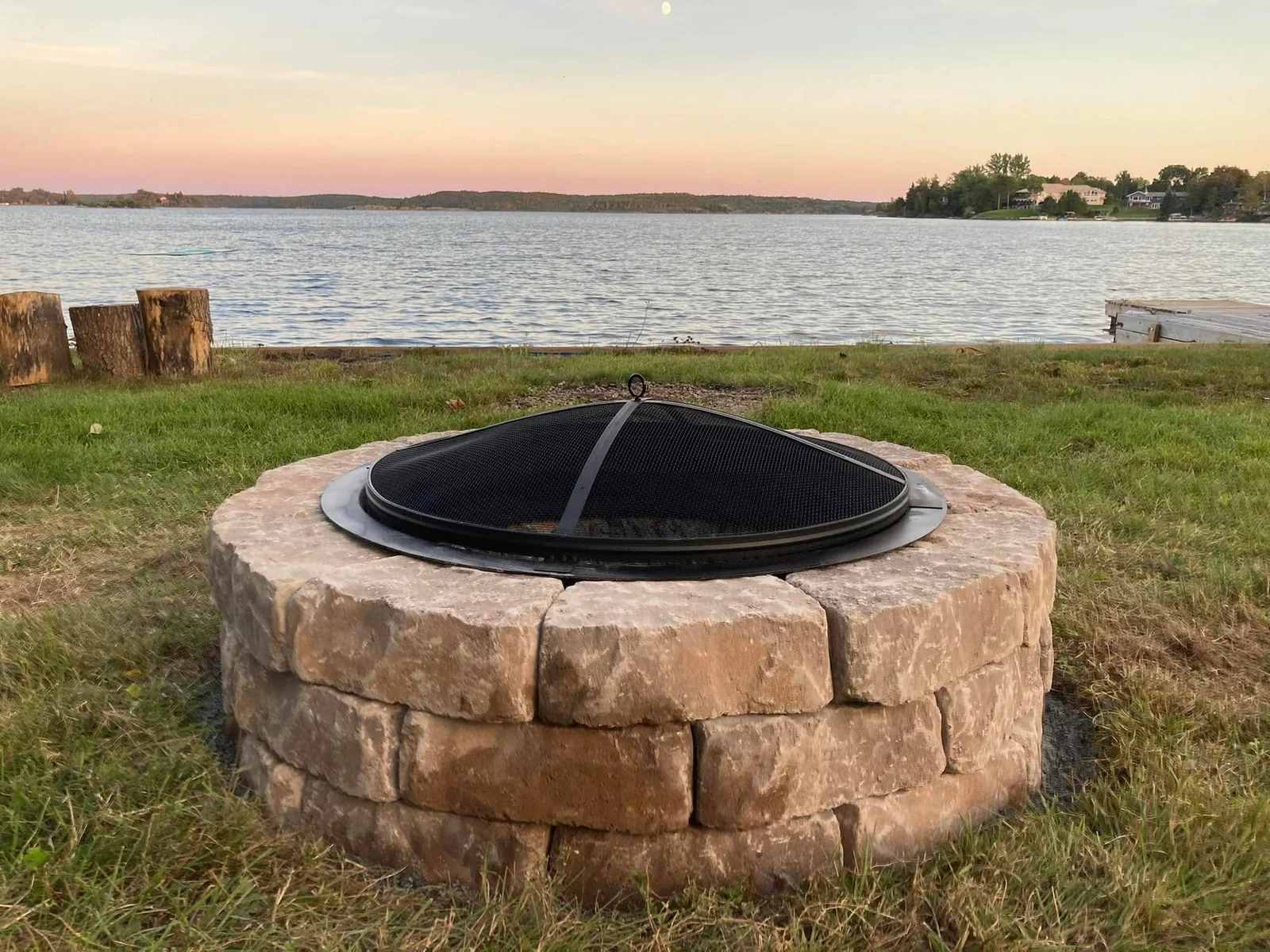 Circular stone firepit beside a lawn overlooking a Northern Ontario lake