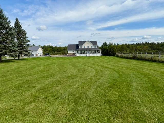Freshly mowed green lawn leading to a country home beneath a blue sky