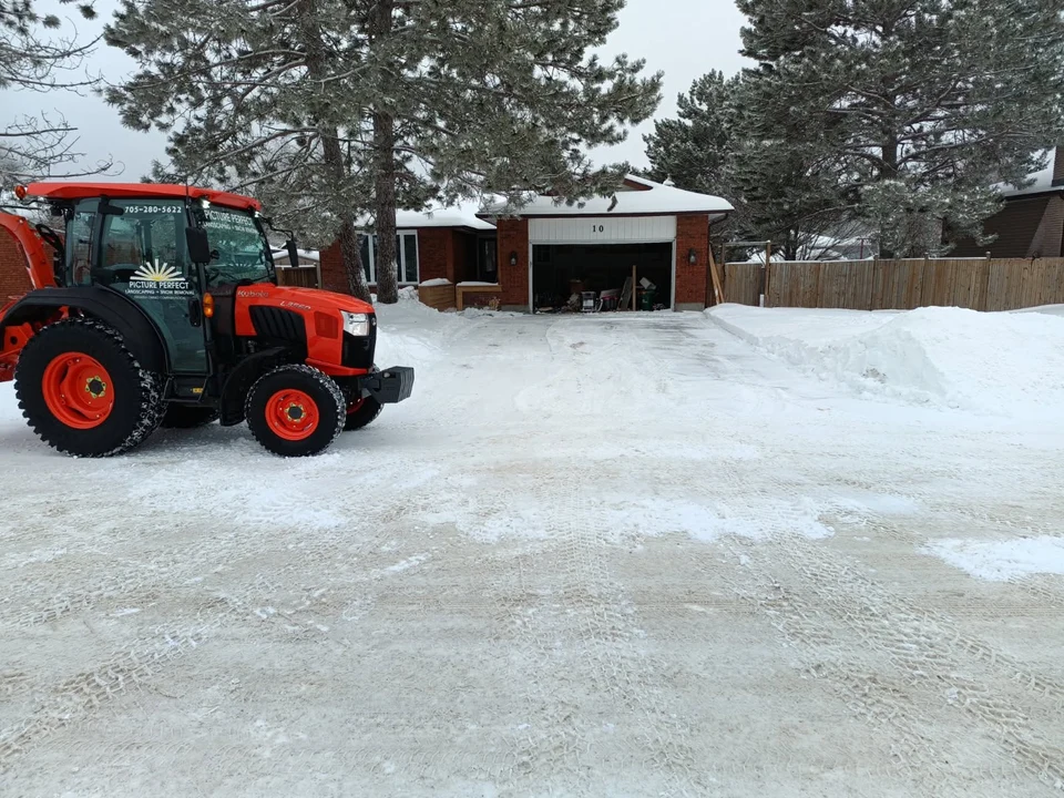 Orange Picture Perfect tractor beside a cleared driveway leading to a residential garage