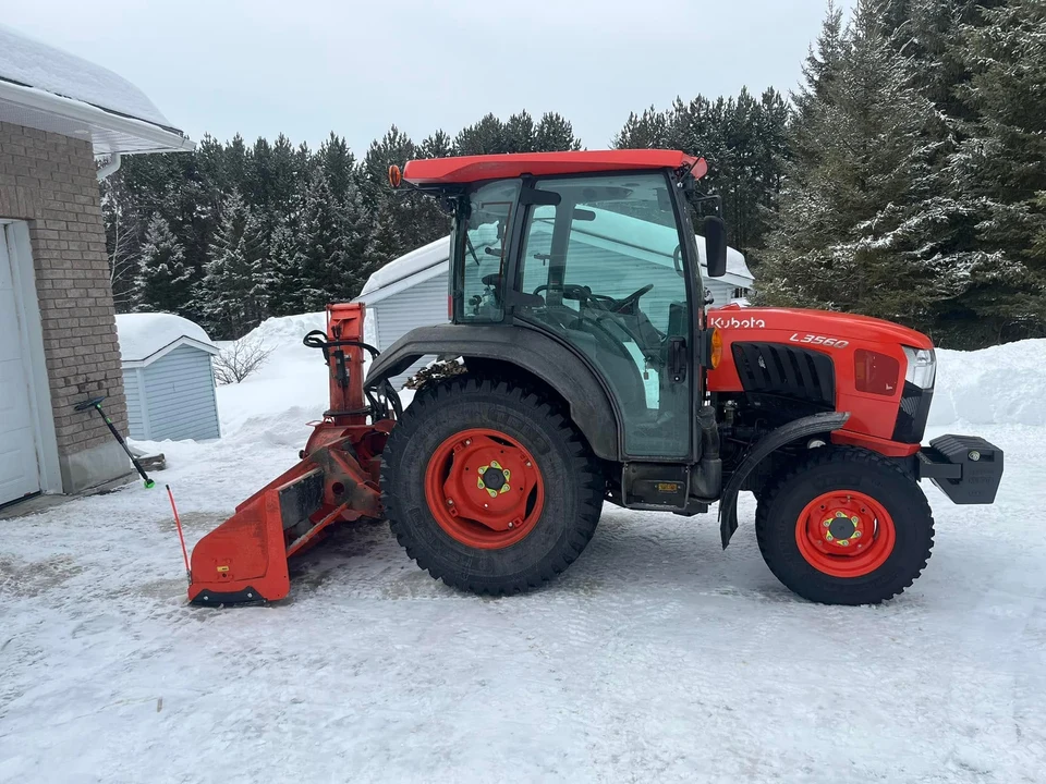 Orange Kubota L3560 tractor with a rear snowblower parked on a snowy residential driveway