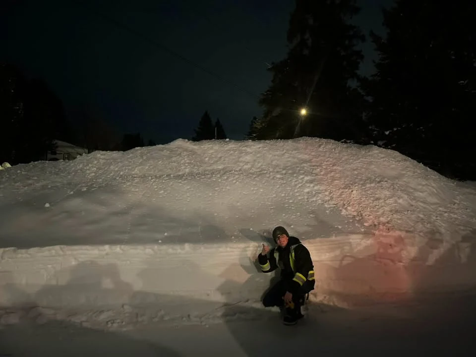 Crew member giving a thumbs-up beside a tall snowbank at night